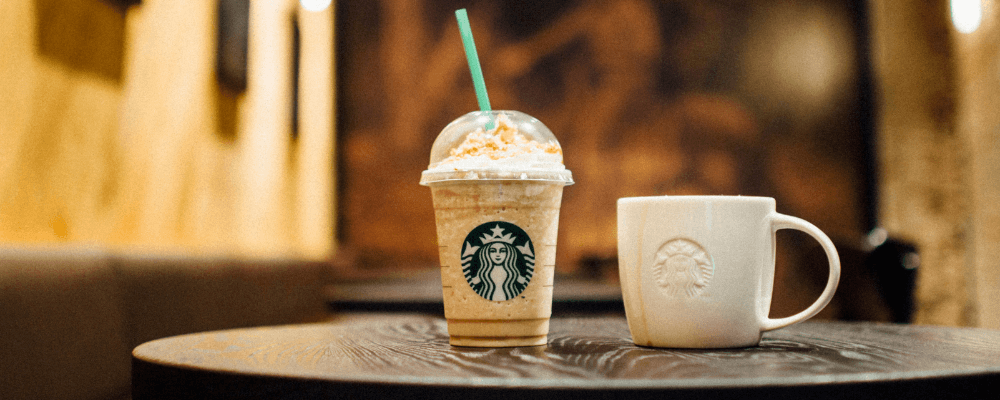 Two starbucks drinks on a table. The takeaway cup showcases the green colour the Starbucks brand uses in their packages.